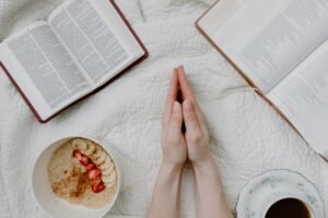 Como Crescer Espiritualmente em Cristo A serene morning scene with a person praying, an open Bible, oatmeal, and coffee.